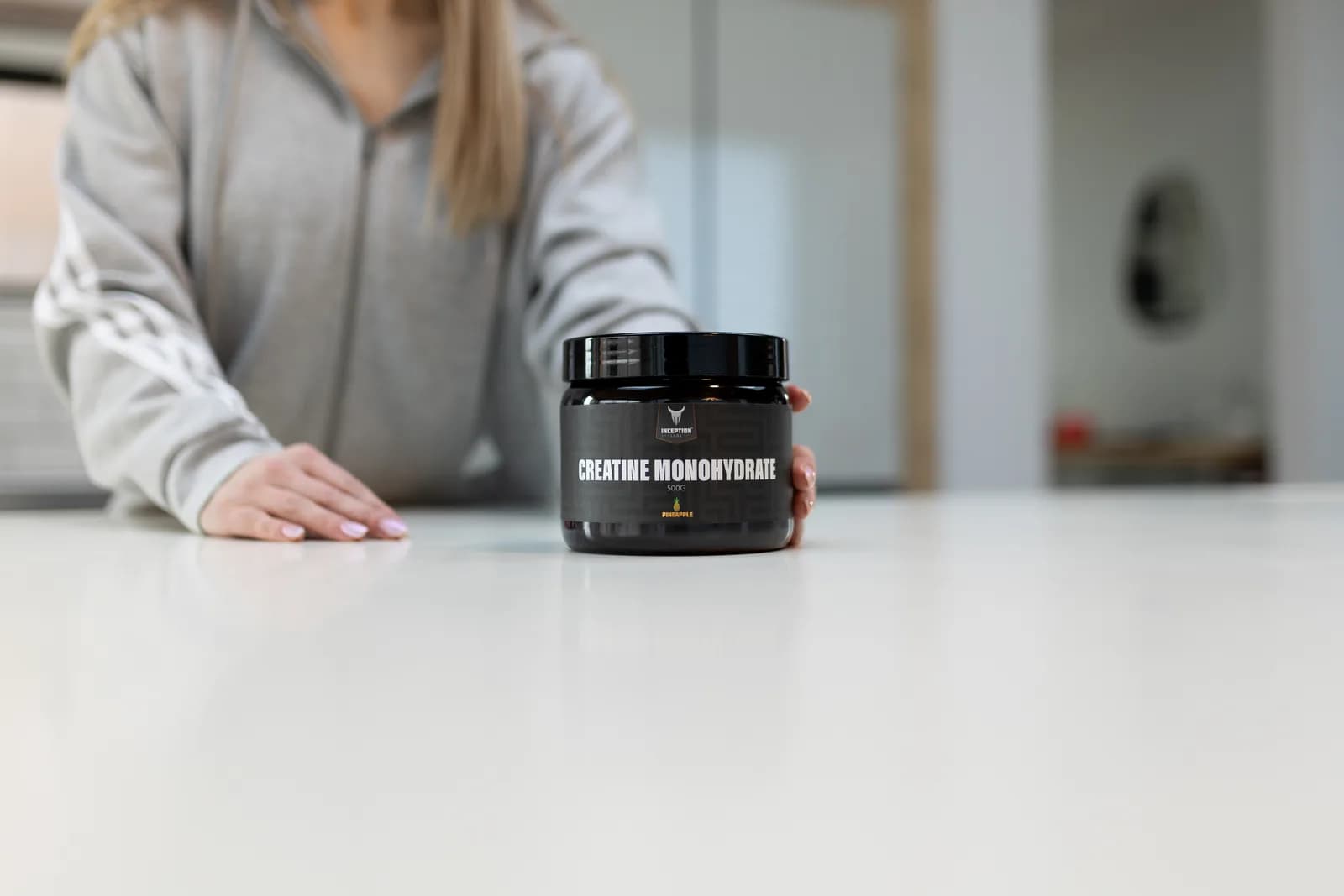 Woman placing a 500g jar of Inception Labs Creatine Monohydrate on a kitchen counter